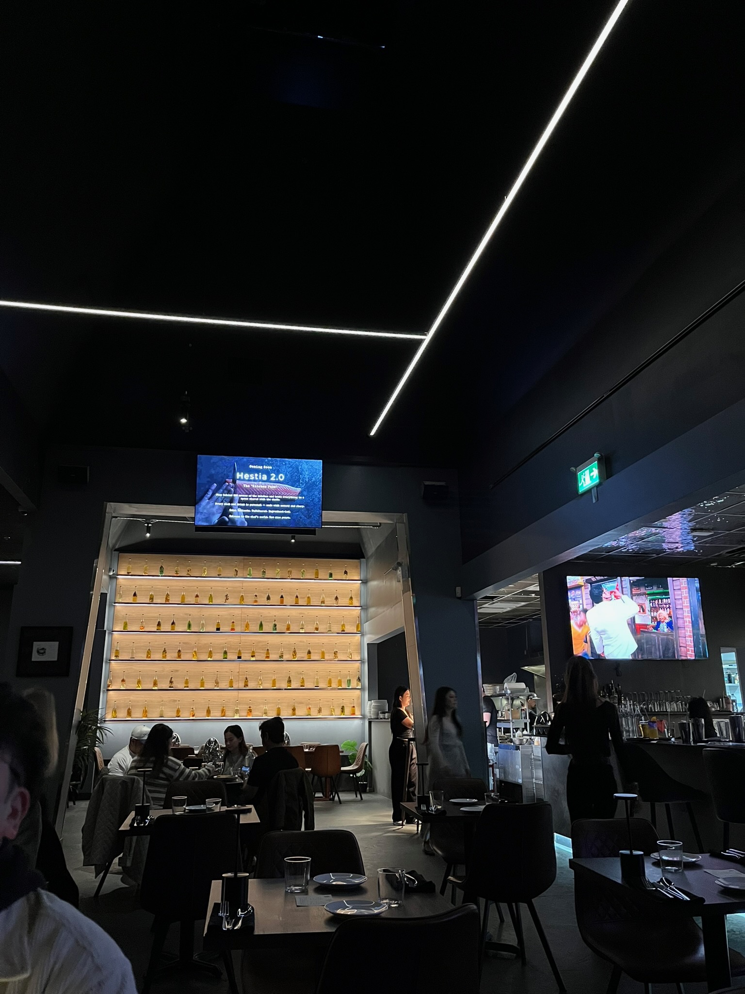 The dining room at Hestia, dark and moody with warm lighting and backlit bottle wall