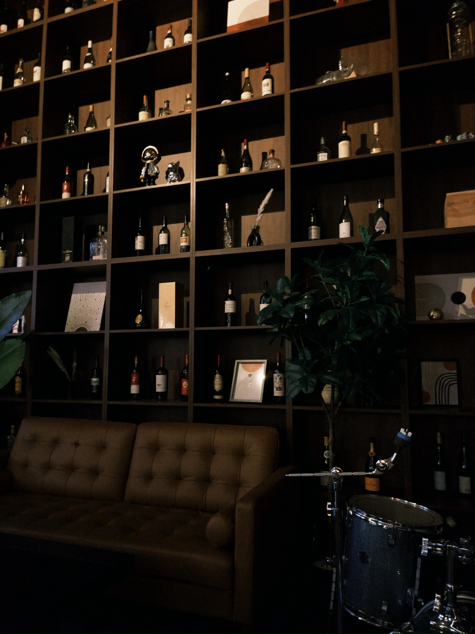 Hestia's lounge area with floor-to-ceiling wine shelf, leather sofa, and drum kit for live music nights