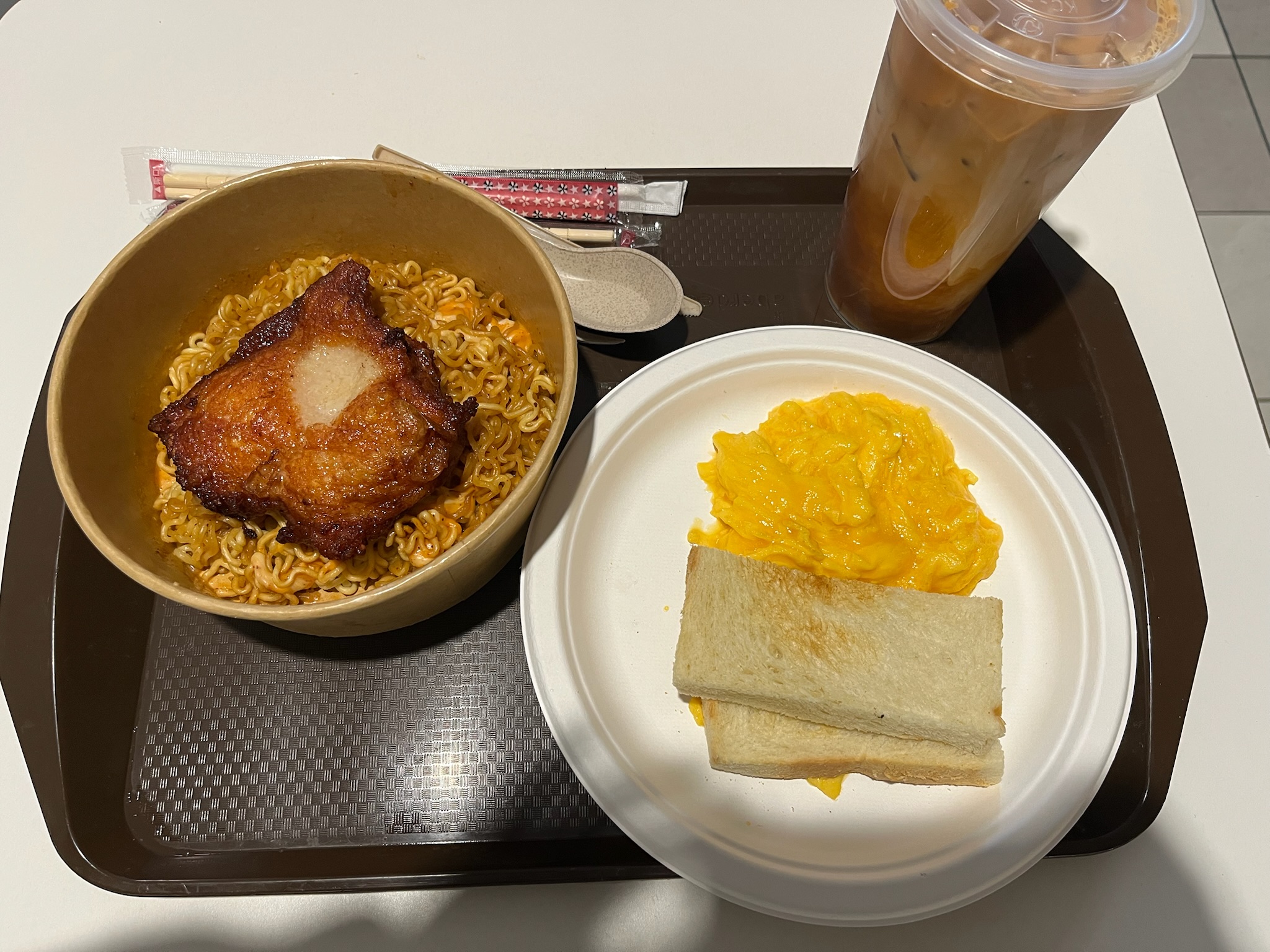 The full Set D tray: Korean instant noodles with chicken cutlet, scrambled eggs, butter toast, and iced milk tea